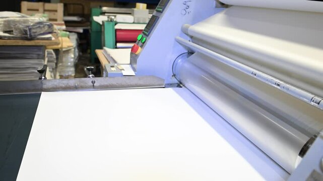 An industrial laminator works by laminating, applying a transparent film to paper in the production room of a printing house