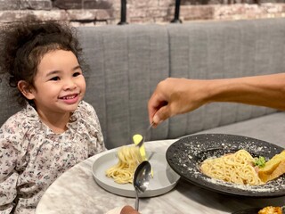 Little girl eating spaghetti with her father in the living room at home