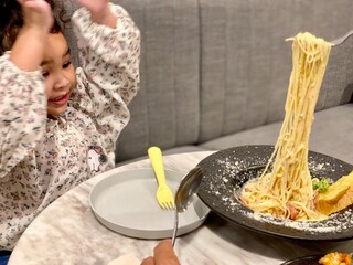 Cute little girl eating spaghetti with her mother at home on the couch