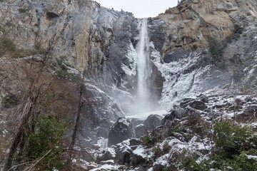 A man visits Yosemite Falls in winter, USA. He is enjoying the view of the waterfall and the...