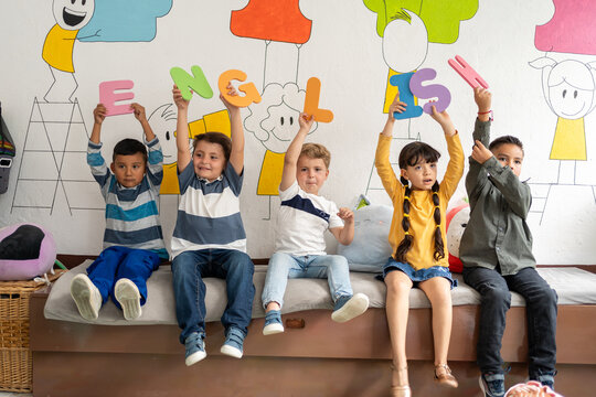Diverse group of preschool children holding large colorful letters spelling “English” in a bright classroom. Early language learning, playful literacy, preschool and kindergarten education