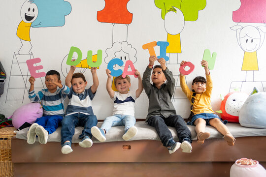 Diverse group of preschool children holding up large colorful letters spelling the word “education”, sitting in a bright classroom. Early literacy, diversity in education, kindergarten learning