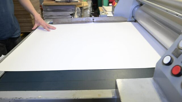 An industrial laminator works by laminating, applying a transparent film to paper in the production room of a printing house