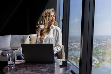 A woman takes pleasure in sipping her warm coffee while diligently working on her sleek laptop in a...