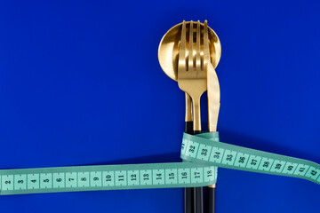 Golden Cutlery Wrapped With Measuring Tape on a Vibrant Blue Background