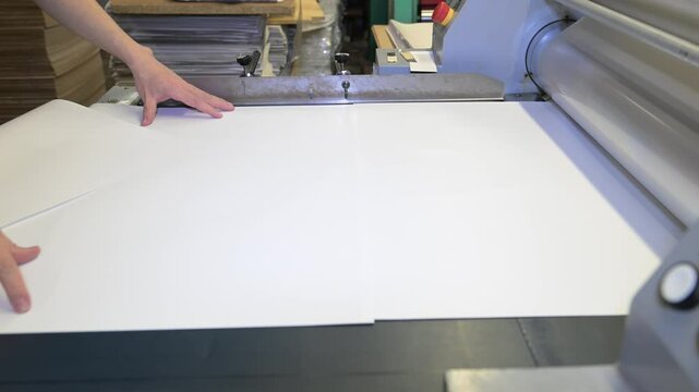 An industrial laminator works by laminating, applying a transparent film to paper in the production room of a printing house