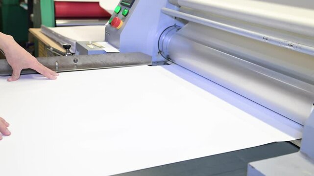 An industrial laminator works by laminating, applying a transparent film to paper in the production room of a printing house
