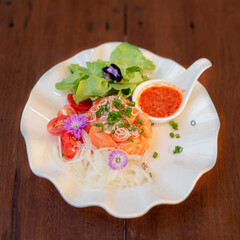 Spicy Thai Salmon Salad with Fresh Vegetables, Vibrant Thai-style salmon salad served on a white petal plate, topped with sliced shallots, herbs, chili sauce, and colorful edible flowers.