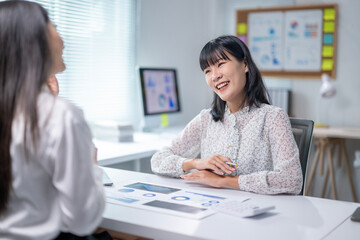 Two women are sitting at a desk with a white board behind them