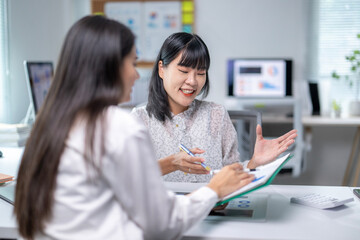 Two women are sitting at a desk, one of them is writing something down