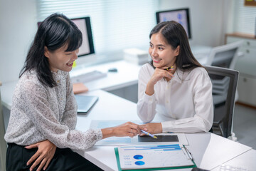 Two women are sitting at a desk, one of them is handing a pen to the other