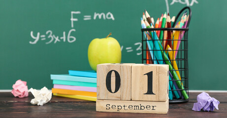 Different stationery, fresh apple and calendar with date SEPTEMBER 1 on wooden table against green...