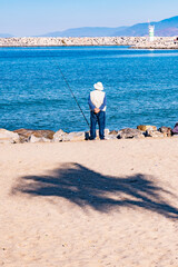 A man is fishing in the ocean with a white hat on