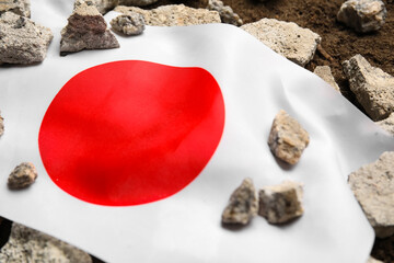 Japanese flag with stone debris on soil. Earthquake concept