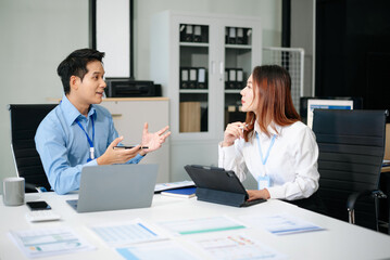 Obraz premium Two young Asian professionals engaged in teamwork and business discussions in modern office embodying corporate