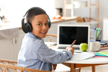 Little African-American boy in headphones studying computer sciences online at home