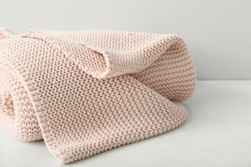 New knitted folded blanket on table near light wall, closeup