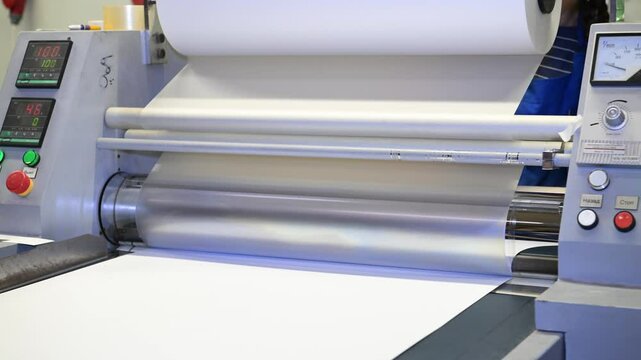 An industrial laminator works by laminating, applying a transparent film to paper in the production room of a printing house