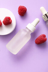Bottle of cosmetic raspberry oil on lilac background