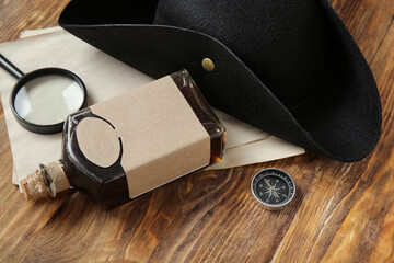 Blank papers with pirate hat, bottle of rum, magnifier and compass on brown wooden background