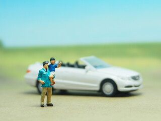 Mini toy of action figure at table with blurred background. Miniature diorama photography concept design. MInifigure of father and son character with car at outdoor. Traveling, holiday and vacation.