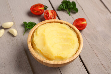Bowl of tasty mashed potatoes with parsley, tomatoes and garlic on grey wooden background