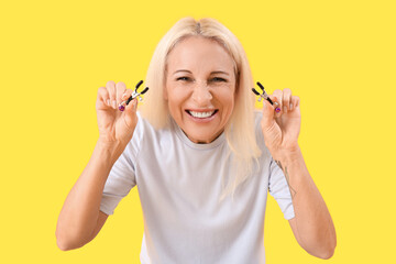 Mature woman with nipple clamps on yellow background