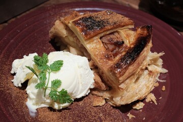 Osaka, March 24, 2024 – Slice of apple pie with golden crust and cinnamon, served with vanilla...