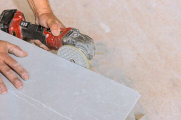 Craftsman is polishing tile stone surface using power tool in construction area filled with dust.
