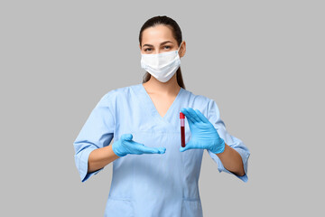 Portrait of female doctor in mask showing test tube with blood sample on grey background