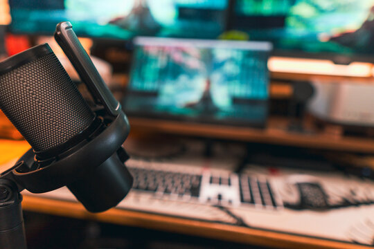 Modern podcast setup with professional microphone on boom arm in cozy home studio, featuring blurred monitors and wooden blinds background. Creative workspace inspiration.