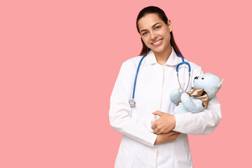 Portrait of female doctor with stethoscope and plush toy on pink background