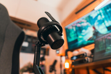 Obraz premium Modern podcast setup with professional microphone on boom arm in cozy home studio, featuring blurred monitors and wooden blinds background. Creative workspace inspiration.