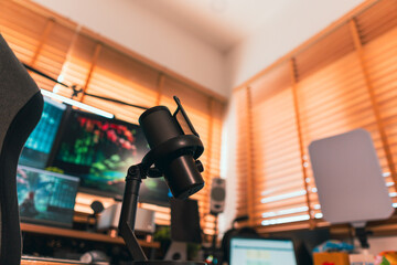 Modern podcast setup with professional microphone on boom arm in cozy home studio, featuring blurred monitors and wooden blinds background. Creative workspace inspiration.