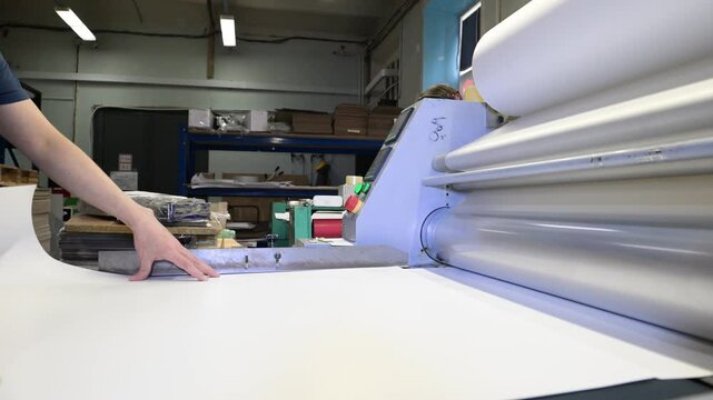 An industrial laminator works by laminating, applying a transparent film to paper in the production room of a printing house