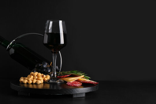 Bottle and glass of red wine with snacks on black background