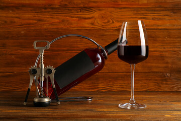 Bottle and glass of red wine with corkscrew on wooden background