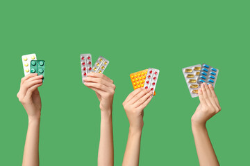 Female hands holding pills in blister packs on green background
