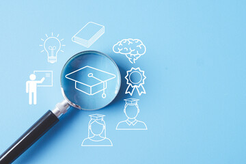Education and learning concept. A magnifying glass focuses on a graduation cap icon among other...