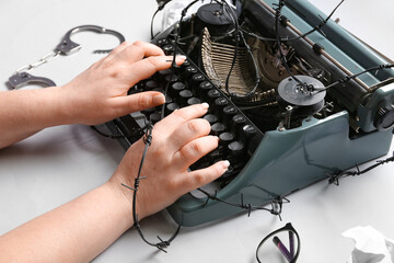Female hands with vintage typewriter, barbed wire and handcuffs on white background. Printing ban...