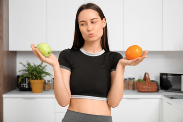 Beautiful young happy woman with fresh apple and orange blowing kiss at home. Weight loss concept