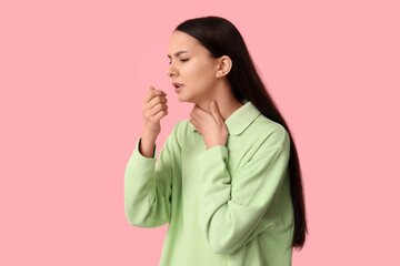 Beautiful young woman suffering from sore throat on pink background