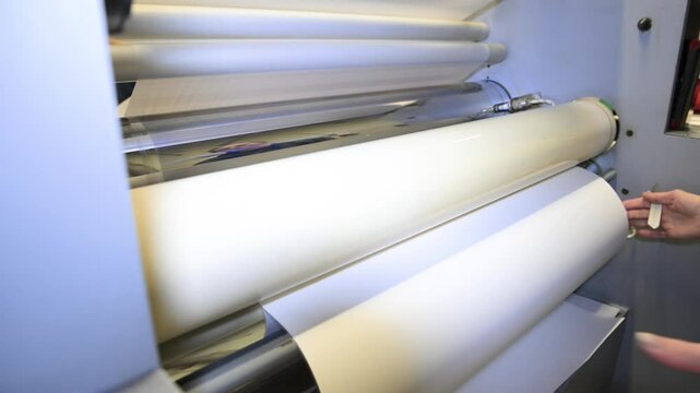 An industrial laminator works by laminating, applying a transparent film to paper in the production room of a printing house