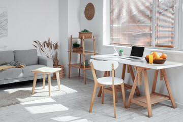 Wicker basket with citruses and laptop on workplace in light room