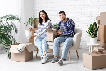 Young happy couple unpacking belongings on white sofa in their new house