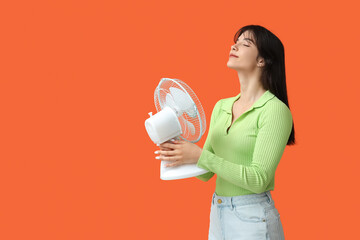 Young woman with electric fan on orange background