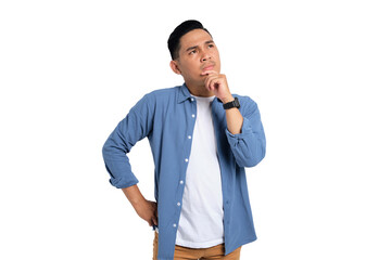 Pensive young Asian man in casual shirt touching his chin, looking up at copy space, having doubts...