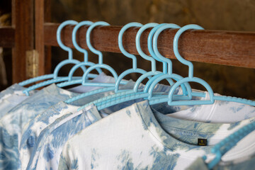 close-up shot of tie-dye t-shirts hanging on light blue plastic hangers. The shirts feature a soft, pastel tie-dye pattern.