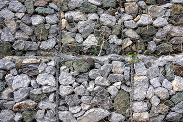gabion wall, showcasing the texture of the grey stones and the wire mesh. The image highlights the detailed pattern and rugged nature