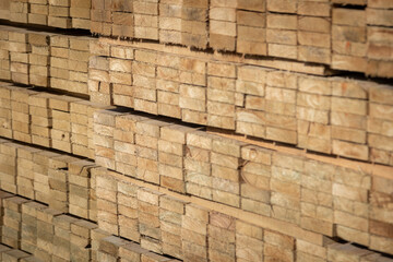 Stacked wooden planks in a lumberyard, showing various shades and textures of the wood, arranged in neat rows.